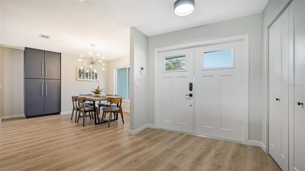 A bright entryway with wood-look flooring leads to a dining area with a modern chandelier — 3924 HELENE STREET, SARASOTA, FL