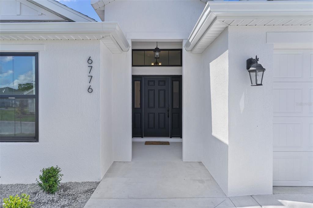 The exterior of a white house features a black front door and house number 6776 — 6776 ROBINETTE RUN RUN UNIT Robinette Run, THE VILLAGES, FL