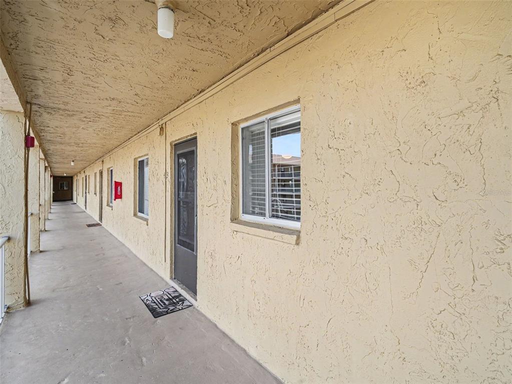 An exterior view of an apartment building walkway with a textured wall and windows — 3801 LAKE BAYSHORE DRIVE UNIT H413, BRADENTON, FL
