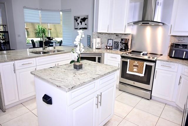 A modern kitchen features white cabinetry, granite countertops, a central island, and stainless steel appliances — 2270 TOURNAMENT COURT, KISSIMMEE, FL