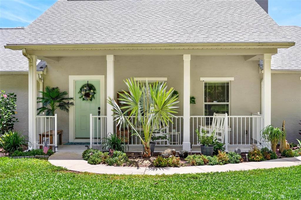 A front porch with a light green door, white railings, and a small palm tree — 12854 NE 118TH TERRACE, OCKLAWAHA, FL