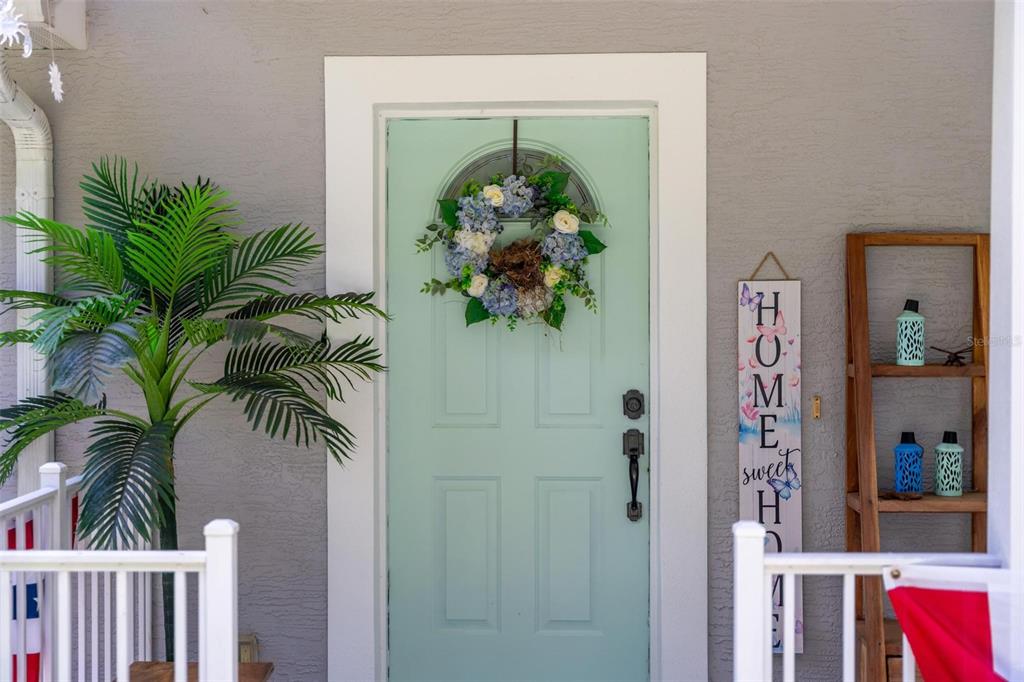 A light blue front door with a floral wreath sits beside a potted palm plant — 12854 NE 118TH TERRACE, OCKLAWAHA, FL