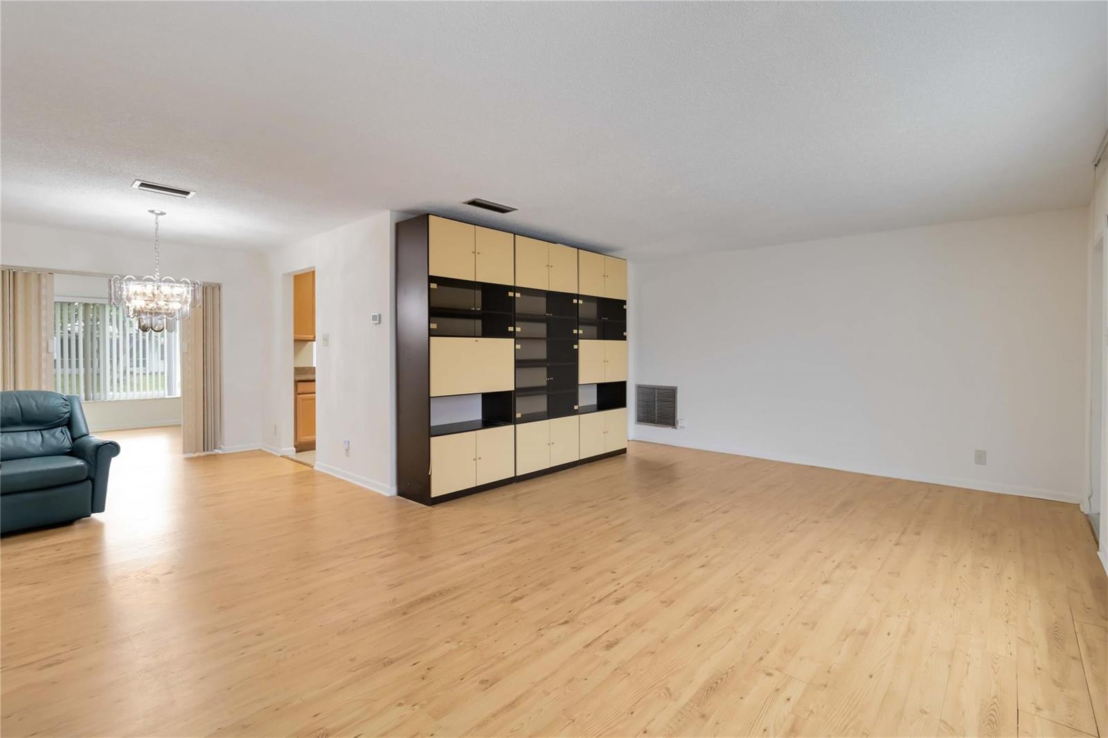 A spacious living room with light wood flooring, white walls, and a large modular storage unit — 735 NW 73rd Terrace, Margate FL 33063, MARGATE, FL