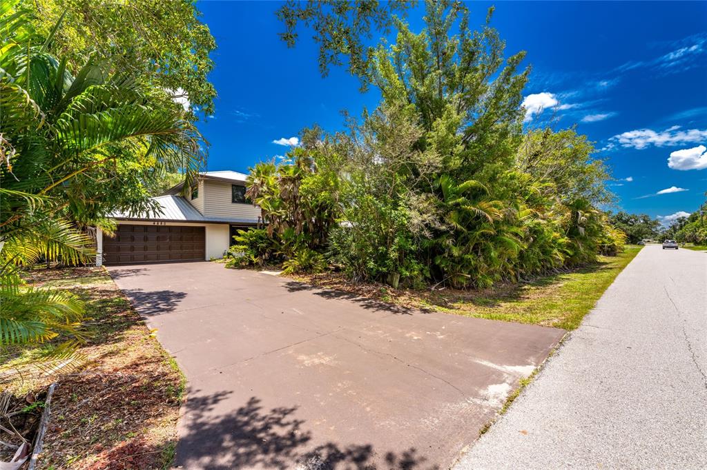 A two-story house with a brown garage and a paved driveway surrounded by lush trees — 4880 WECOMA AVENUE, NORTH PORT, FL