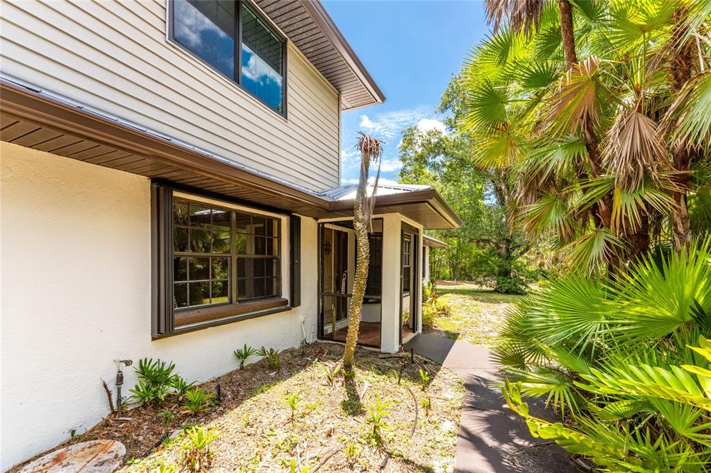The exterior of a two-story home features a screened entryway and surrounding palm trees — 4880 WECOMA AVENUE, NORTH PORT, FL