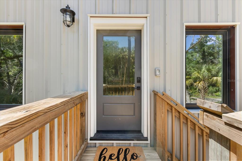 A two-story metal-sided building features an elevated wooden staircase and deck in a wooded area — 10408 W LARCHWOOD STREET, HOMOSASSA, FL