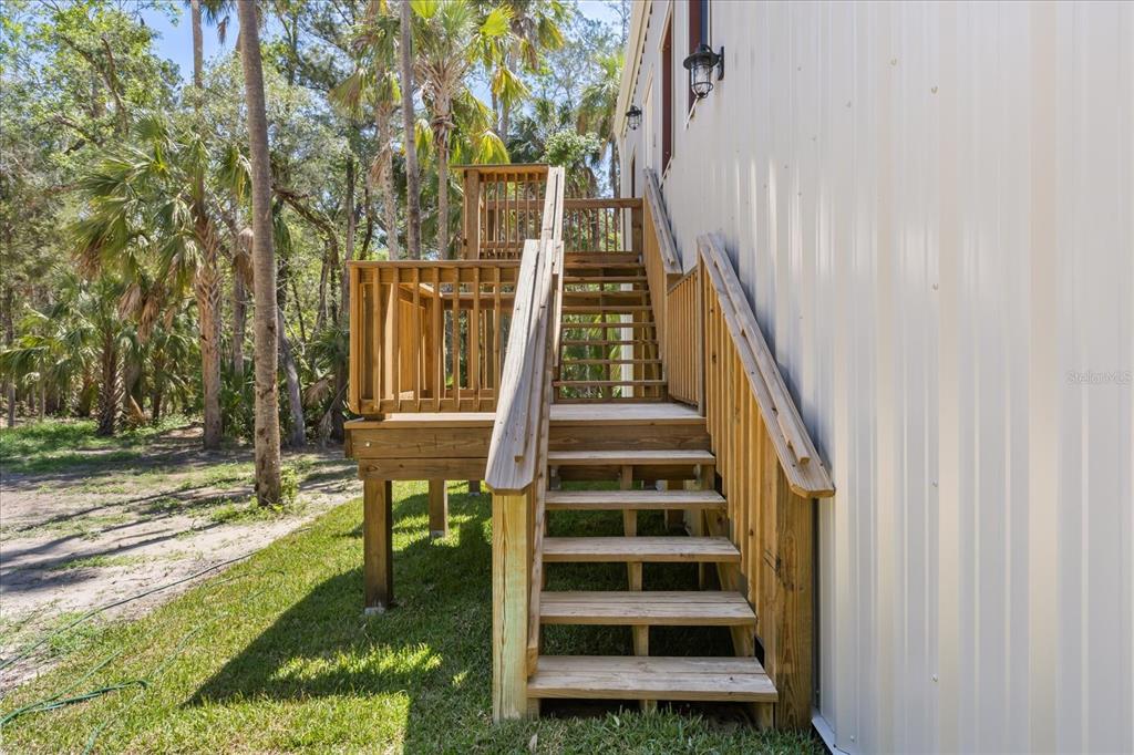 A light-colored metal building features a wooden staircase leading to an elevated deck and entrance — 10408 W LARCHWOOD STREET, HOMOSASSA, FL