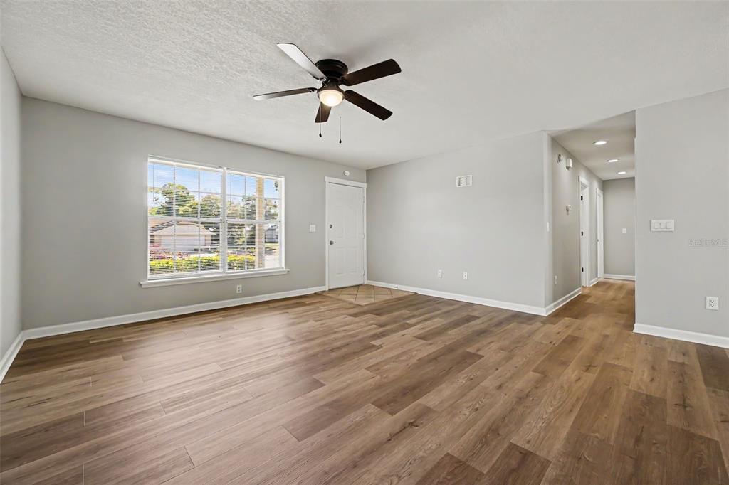 An empty living room features light gray walls, wood-look flooring, a ceiling fan, and windows — 756 SHAFTON AVENUE, DELTONA, FL