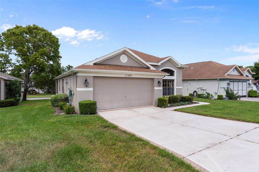 A single-story house with a beige stucco exterior, a two-car garage, and a concrete driveway — 11293 COPLEY COURT, SPRING HILL, FL