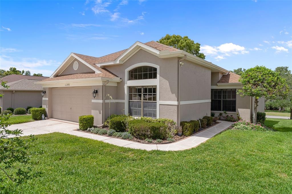 A tan single-story house with a two-car garage and a landscaped front yard — 11293 COPLEY COURT, SPRING HILL, FL