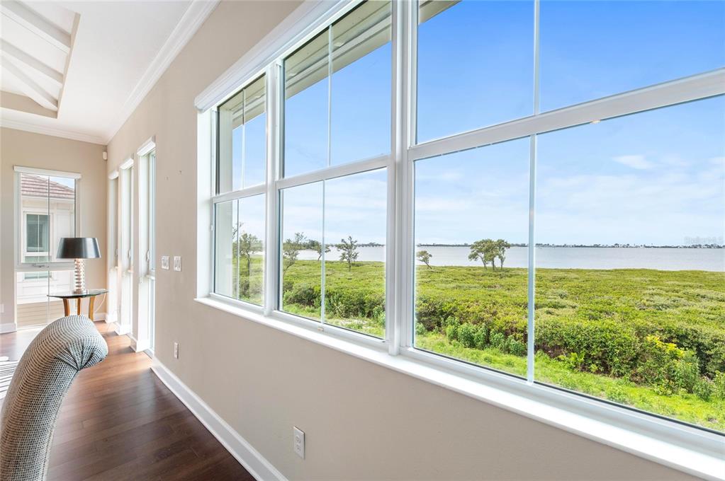 A bright room with hardwood floors features large windows overlooking a grassy field and water — 342 CASTAWAY CAY DRIVE UNIT 201, BRADENTON, FL