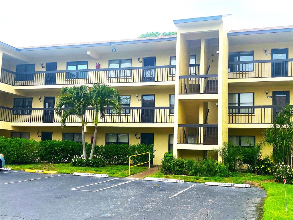 A three-story yellow apartment building with exterior walkways and a parking lot in front — 425 30TH AVENUE W UNIT C211, BRADENTON, FL
