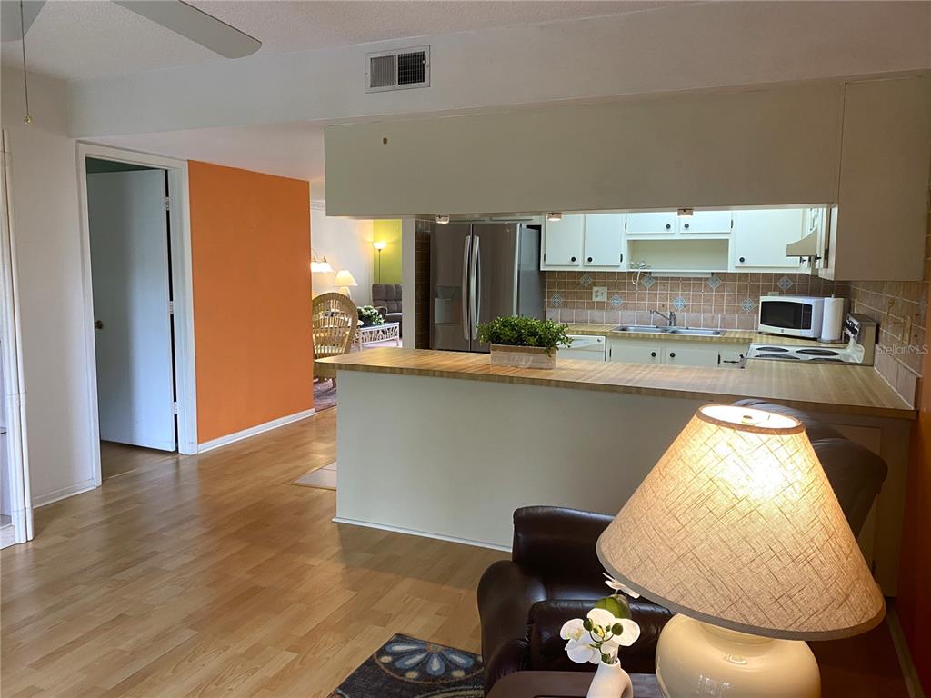 A kitchen with a breakfast bar overlooks a living area with light wood flooring — 425 30TH AVENUE W UNIT C211, BRADENTON, FL