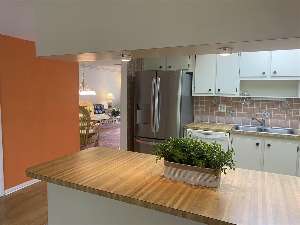 A kitchen with a wood-look countertop island, stainless steel refrigerator, and view into a dining area — 425 30TH AVENUE W UNIT C211, BRADENTON, FL