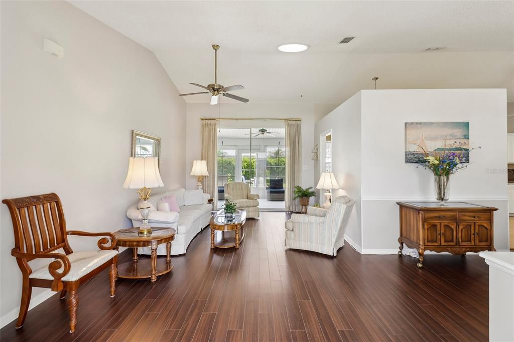 A living room with dark wood floors, vaulted ceilings, and a view of a screened patio — 4529 PEACH TREE STREET, LEESBURG, FL