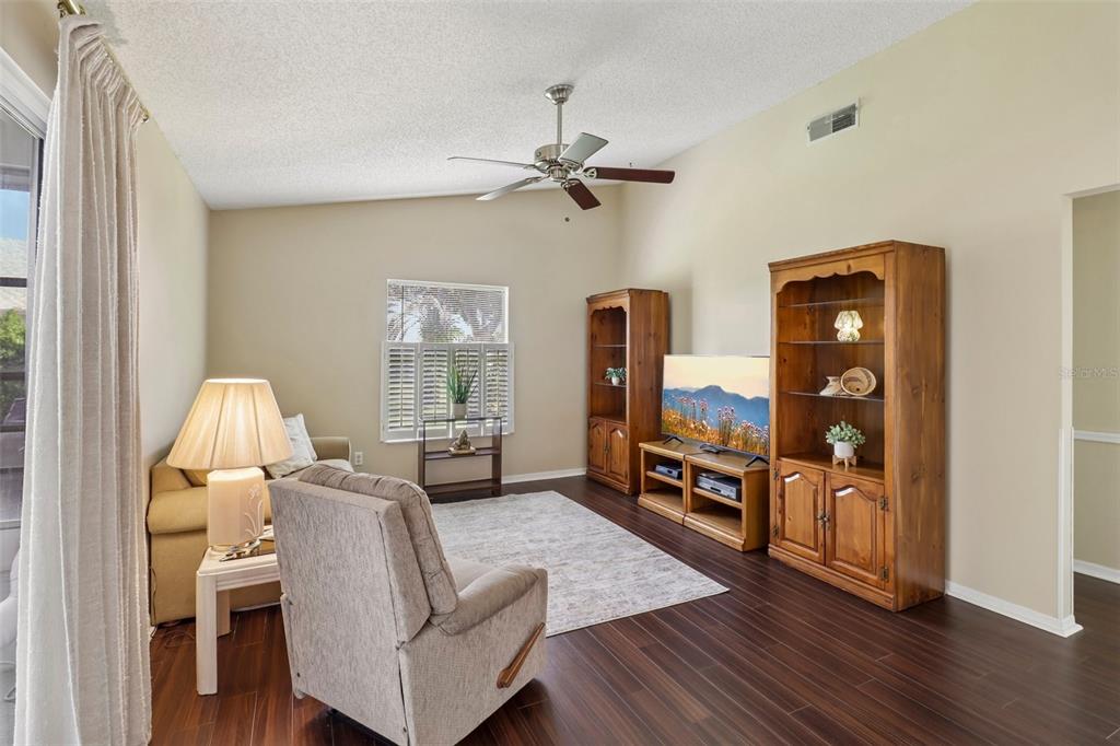 A living room features dark wood flooring, a vaulted ceiling with a fan, and wooden shelving — 4529 PEACH TREE STREET, LEESBURG, FL