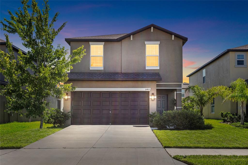 A two-story house with a two-car garage and a concrete driveway at dusk — 6402 BACK FORTY LOOP, ZEPHYRHILLS, FL