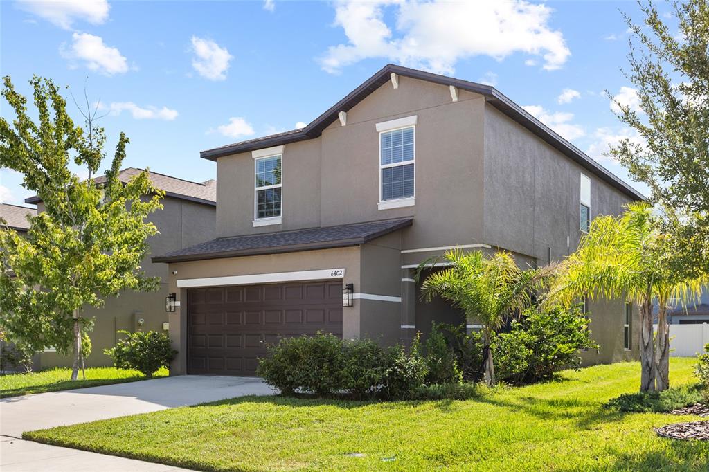 A two-story house with a brown garage, stucco exterior, and a green lawn — 6402 BACK FORTY LOOP, ZEPHYRHILLS, FL