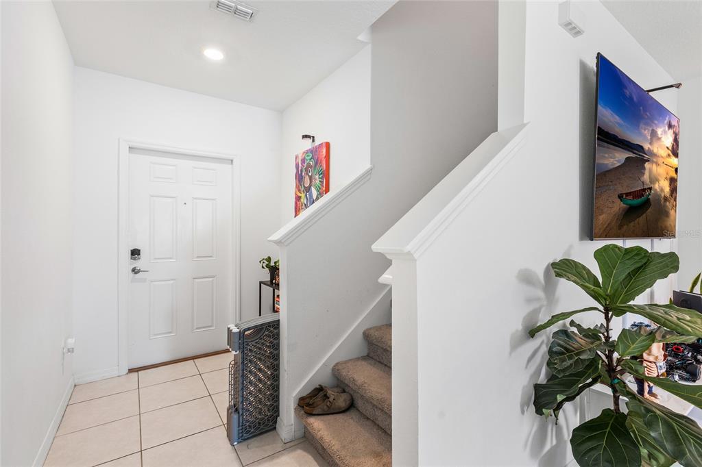 An entryway features tiled flooring, a white front door, and carpeted stairs leading upward — 6402 BACK FORTY LOOP, ZEPHYRHILLS, FL