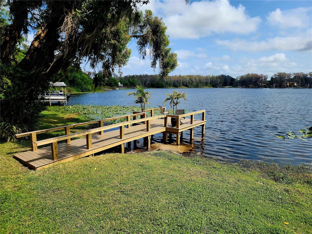 A wooden dock extends from a grassy lawn into a lake with lily pads — 3402 ELLENWOOD LANE, TAMPA, FL