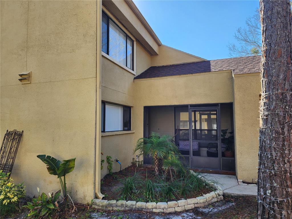A two-story stucco building exterior features a screened-in porch and a small landscaped garden — 3402 ELLENWOOD LANE, TAMPA, FL