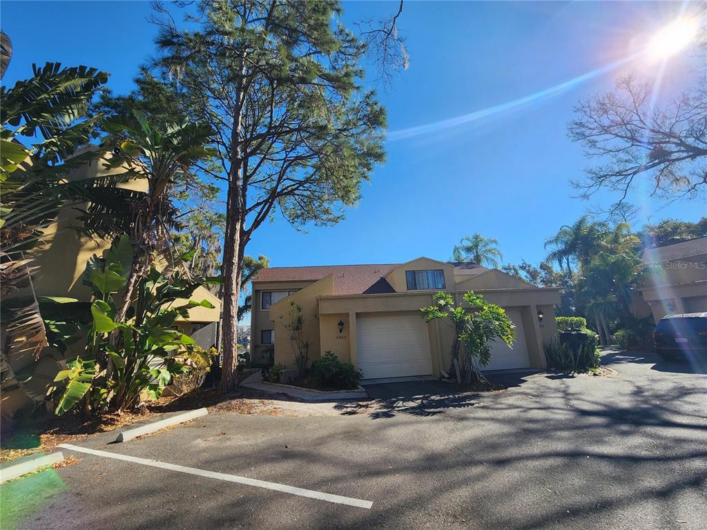 A two-story tan townhouse with a two-car garage and surrounding trees under a blue sky — 3402 ELLENWOOD LANE, TAMPA, FL