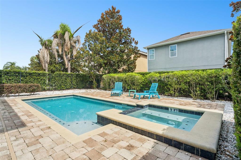 A backyard swimming pool and attached spa are surrounded by a paved patio and hedges — 7605 BROOKHURST LANE, KISSIMMEE, FL