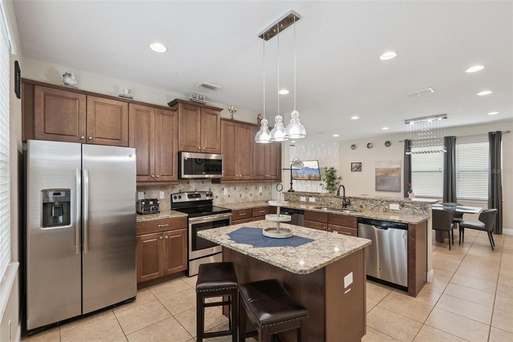 A kitchen features wood cabinets, granite countertops, stainless steel appliances, and a central island — 7605 BROOKHURST LANE, KISSIMMEE, FL