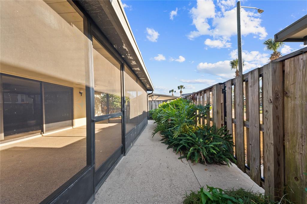 A concrete walkway runs between a screened-in patio and a wooden privacy fence — 2920 PECAN AVENUE, LEESBURG, FL