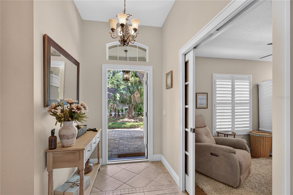 A tiled entryway features a console table, a chandelier, and a doorway leading outside — 16720 BEAUCLAIRE CT, TAVARES, FL
