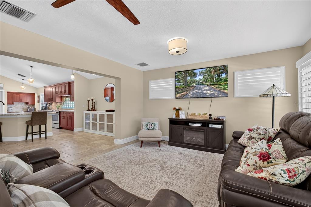 A living room with a brown leather sofa, television, and an open kitchen in the background — 16720 BEAUCLAIRE CT, TAVARES, FL