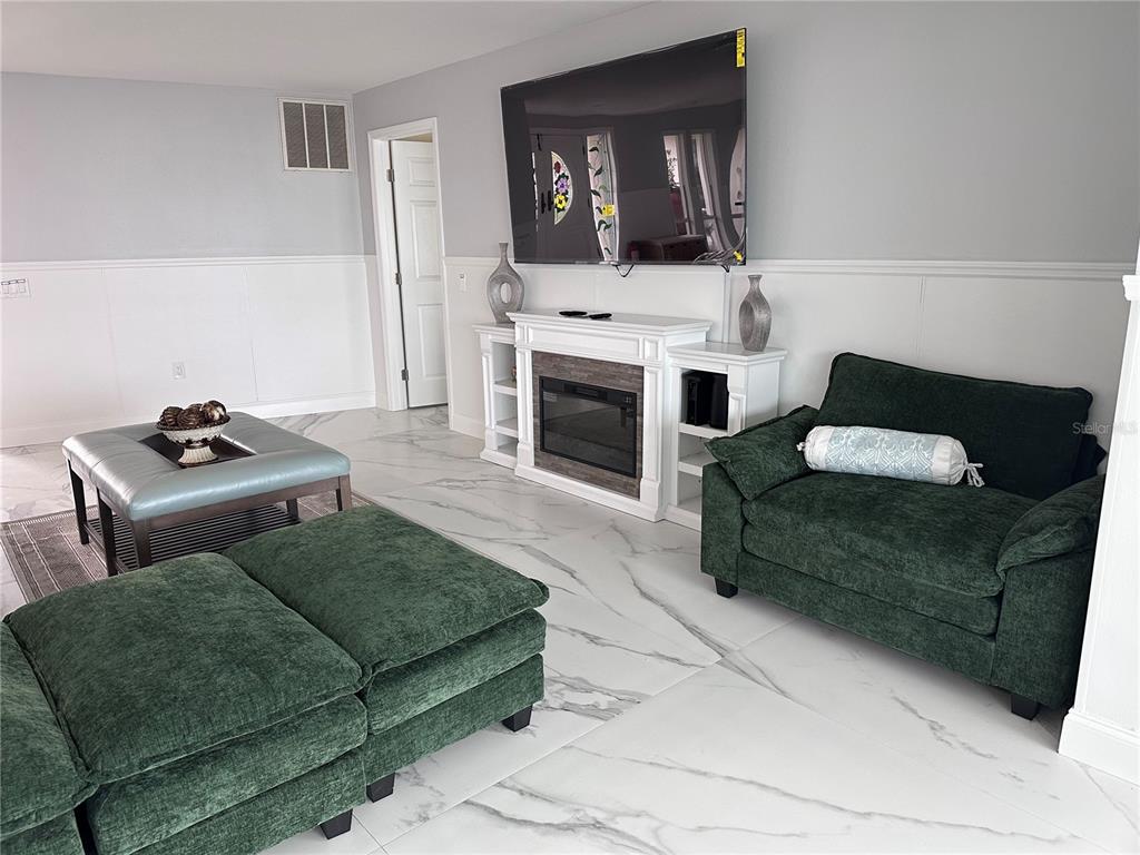 A living room features green furniture, a fireplace, a wall-mounted television, and marble-look tile flooring — 12000 W BAYSHORE DRIVE, CRYSTAL RIVER, FL