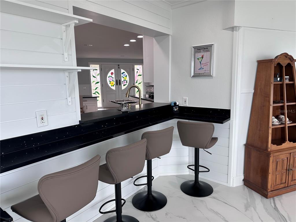 A kitchen breakfast bar features black countertops, three gray stools, and white shiplap walls — 12000 W BAYSHORE DRIVE, CRYSTAL RIVER, FL