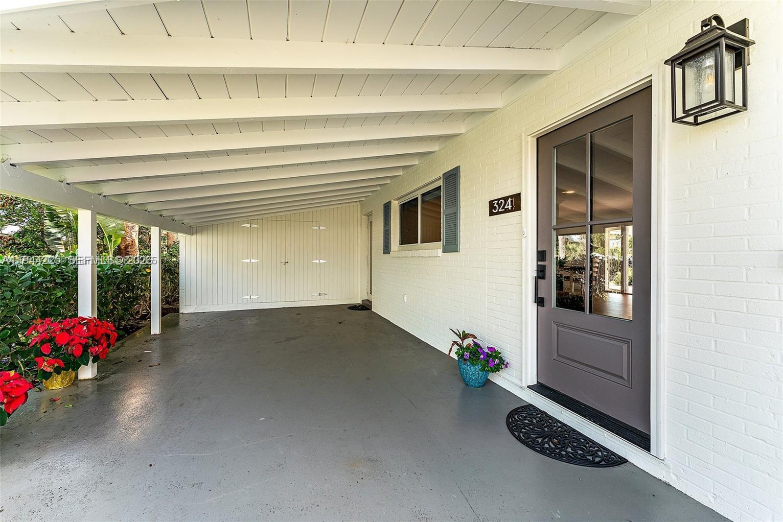 A covered entryway features a gray concrete floor, a brown front door, and white brick walls — 324 Tequesta, Tequesta FL 33469, TEQUESTA, FL