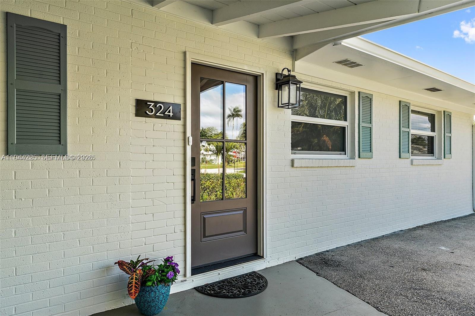 The exterior of a white brick house features a brown front door and green shutters — 324 Tequesta, Tequesta FL 33469, TEQUESTA, FL