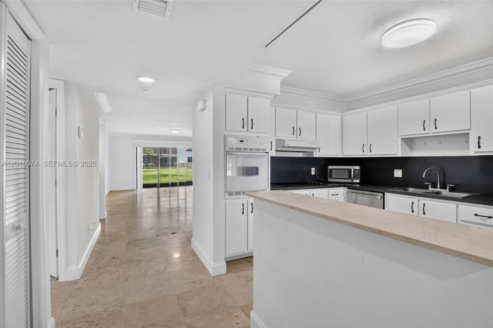 A kitchen with white cabinets and a breakfast bar overlooks an open living area — 359 Lakeview Dr # 102, Weston FL 33326, WESTON, FL