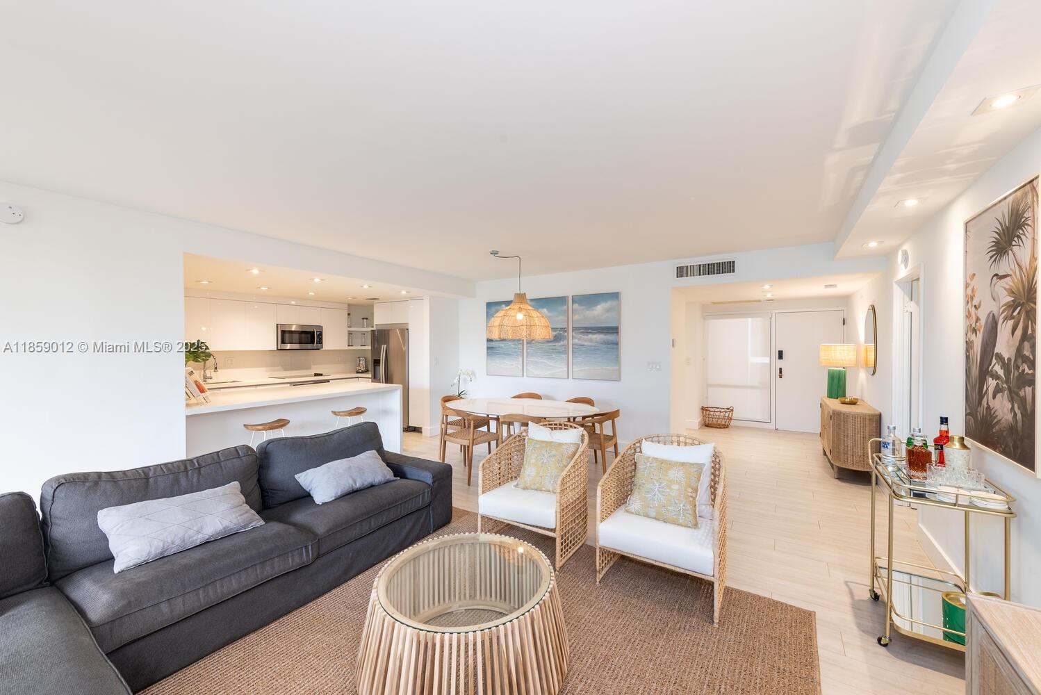 An open-concept living and dining area features a grey sofa, rattan chairs, and white cabinetry — 181 Crandon Blvd # 306, Key Biscayne FL 33149, KEY BISCAYNE, FL