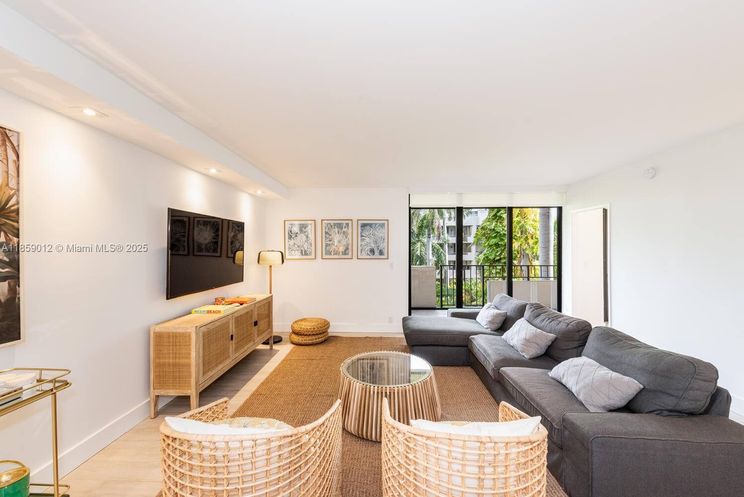 A living room features a grey sectional sofa, rattan chairs, and a wooden media console — 181 Crandon Blvd # 306, Key Biscayne FL 33149, KEY BISCAYNE, FL