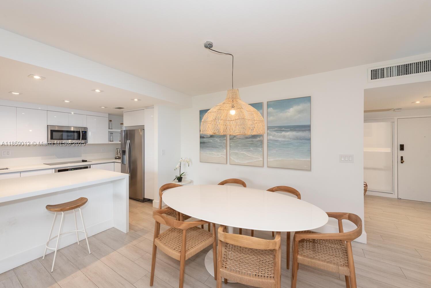 A modern kitchen and dining area feature white cabinetry, a central island, and woven chairs — 181 Crandon Blvd # 306, Key Biscayne FL 33149, KEY BISCAYNE, FL
