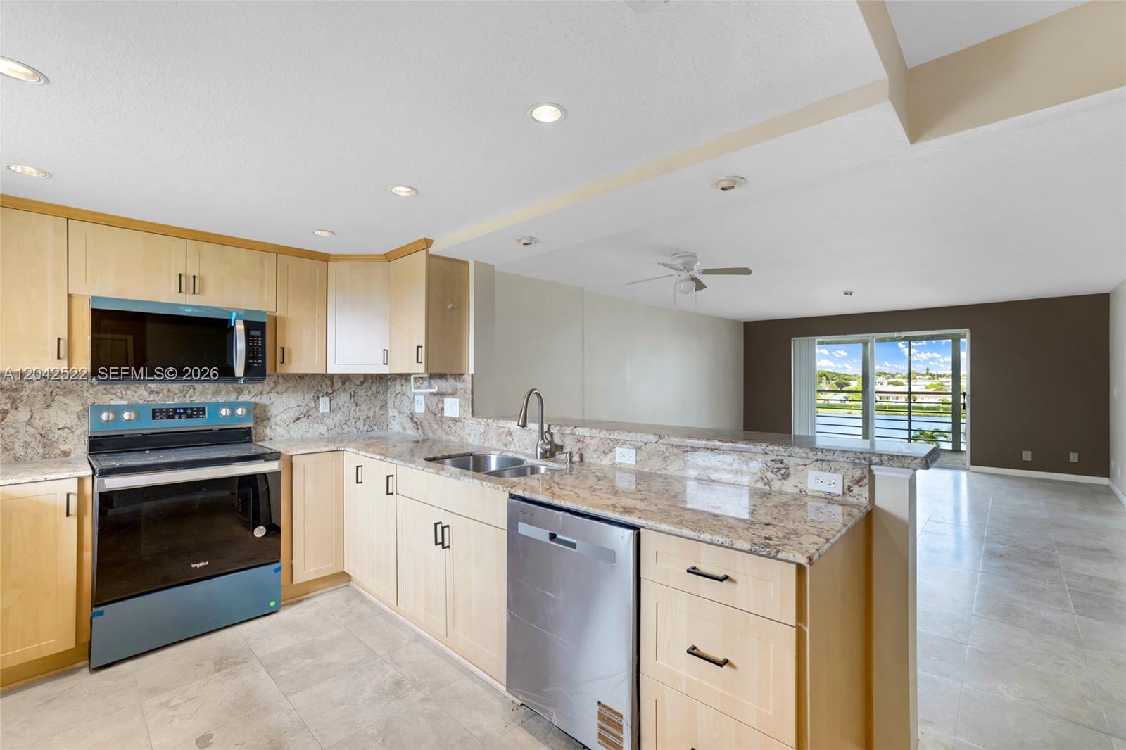 A kitchen with light wood cabinets, granite countertops, and stainless steel appliances overlooks a living area — 321 SE 3rd St # 408, Dania Beach FL 33004, DANIA BEACH, FL