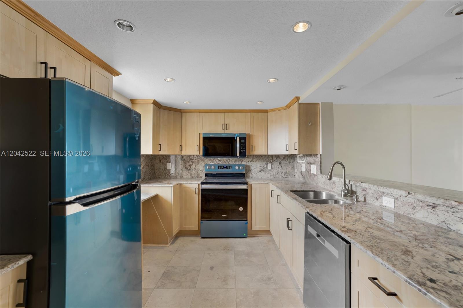 A kitchen features light wood cabinets, granite countertops, a blue refrigerator, and stainless steel appliances — 321 SE 3rd St # 408, Dania Beach FL 33004, DANIA BEACH, FL