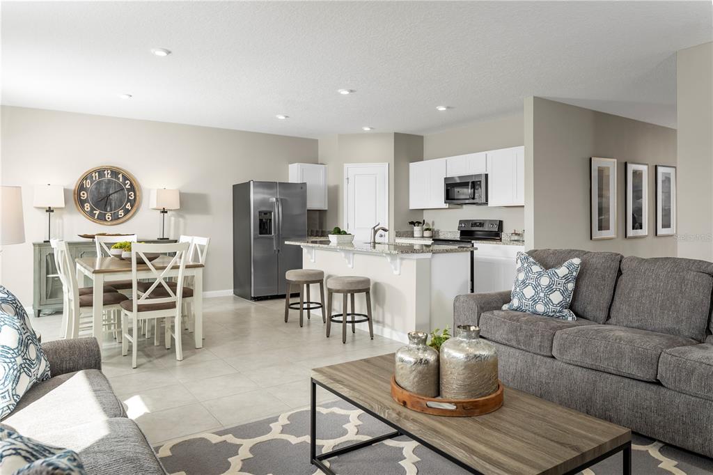 An open-concept living room and kitchen feature gray sofas, a dining area, and white cabinetry — 1113 LEXINGTON LANE, HAINES CITY, FL