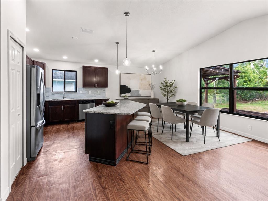 A kitchen and dining area featuring dark wood cabinets, a granite island, and wood flooring — 5011 LEON DRIVE, PALMETTO, FL