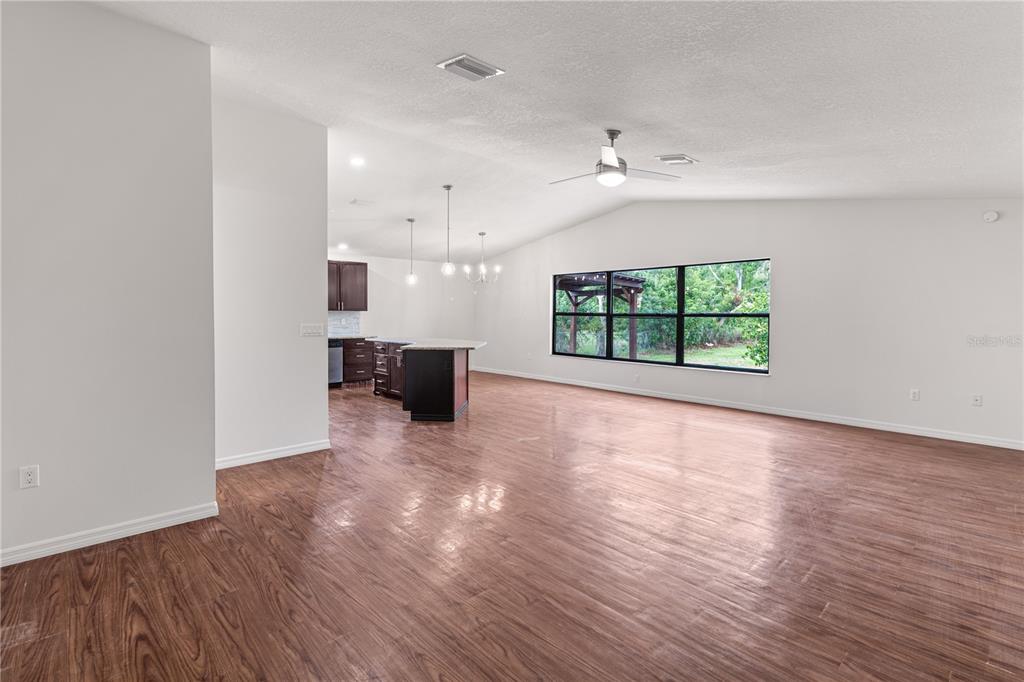 An open-concept living and dining area features dark wood flooring, a kitchen island, and neutral furniture — 5011 LEON DRIVE, PALMETTO, FL