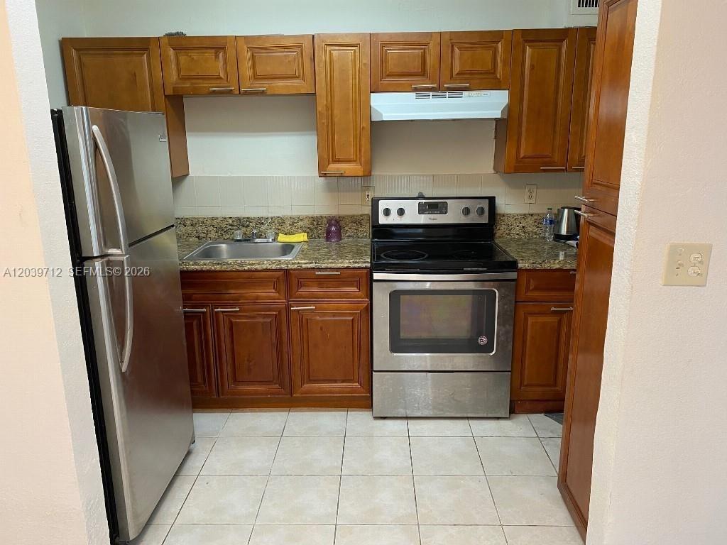 A kitchen features stainless steel appliances, wood cabinets, and granite countertops over tile flooring — 4717 SW 33rd Ave # 102, Dania Beach FL 33312, DANIA BEACH, FL