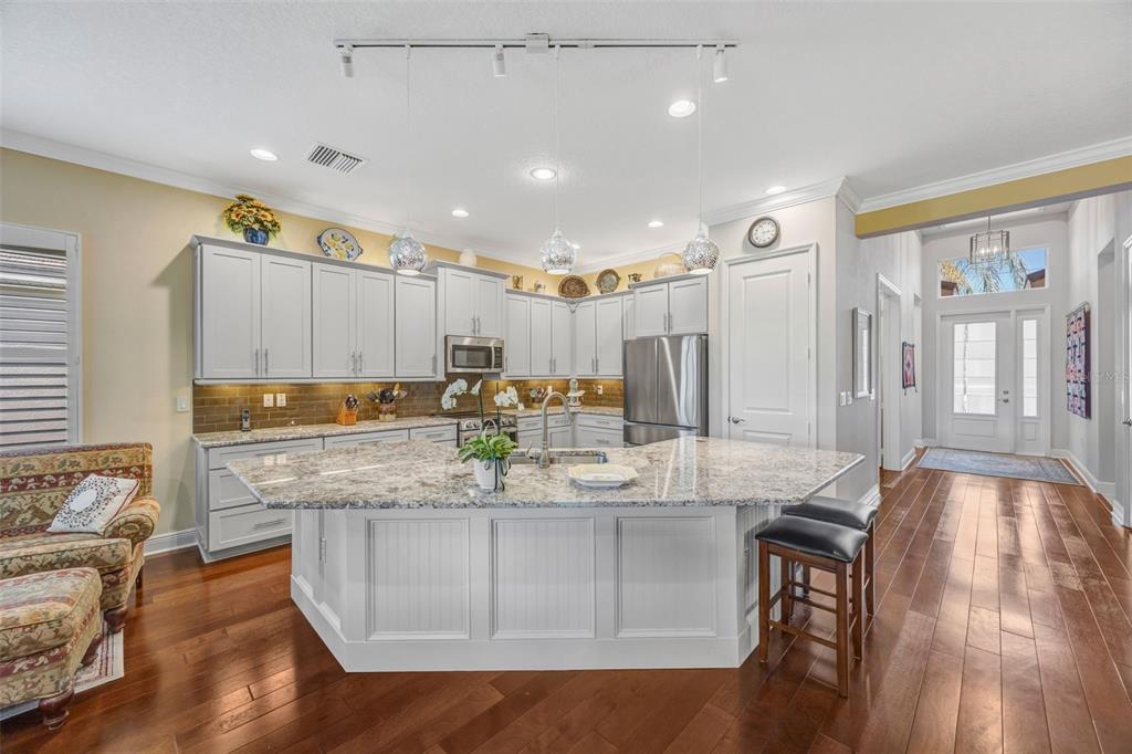 A kitchen features a large granite-topped island, white cabinetry, and hardwood floors — 2415 OAKWOOD PRESERVE DRIVE, WESLEY CHAPEL, FL