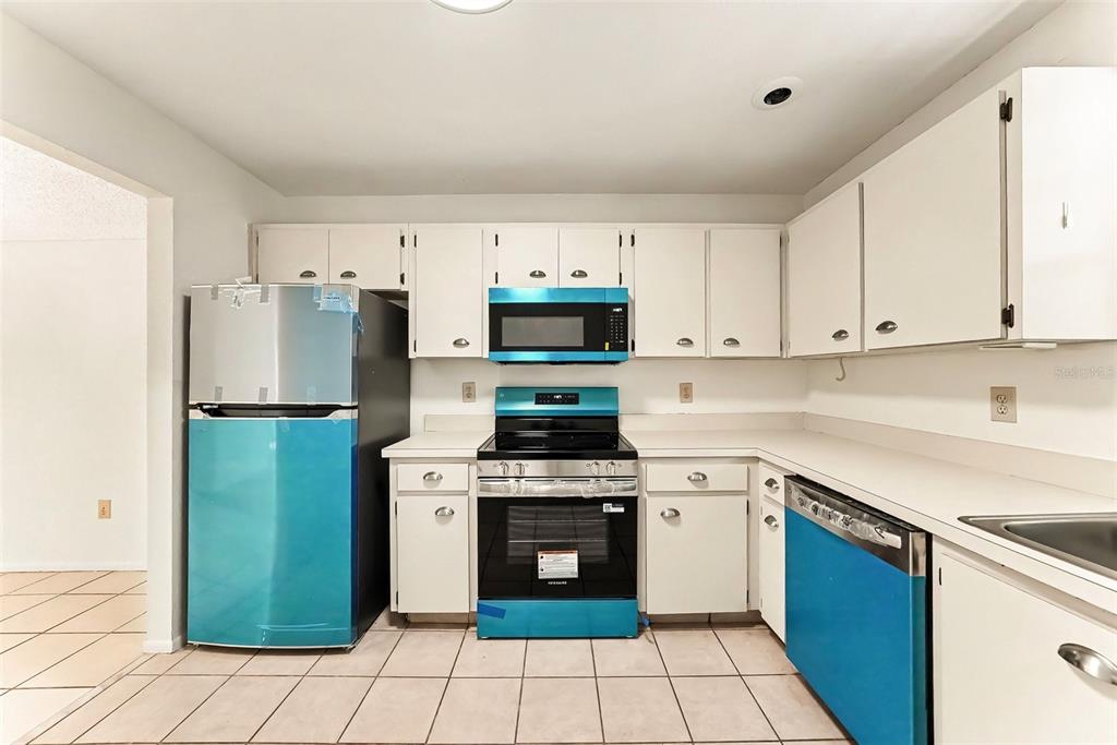 A kitchen features white cabinets, a black stove, a microwave, and stainless steel appliances — 11805 SKYLAKE PLACE UNIT C, TAMPA, FL