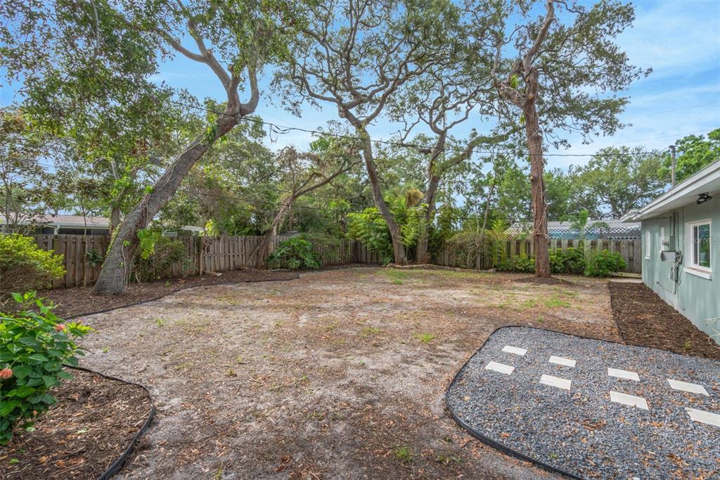 A backyard features a gravel patio area, mature trees, and a wooden privacy fence — 19 VENTURA DRIVE, DUNEDIN, FL
