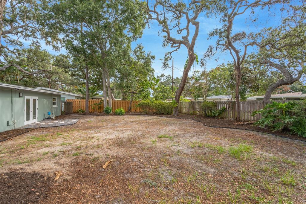 A backyard with sandy ground, mature trees, and a wooden fence surrounding the property — 19 VENTURA DRIVE, DUNEDIN, FL