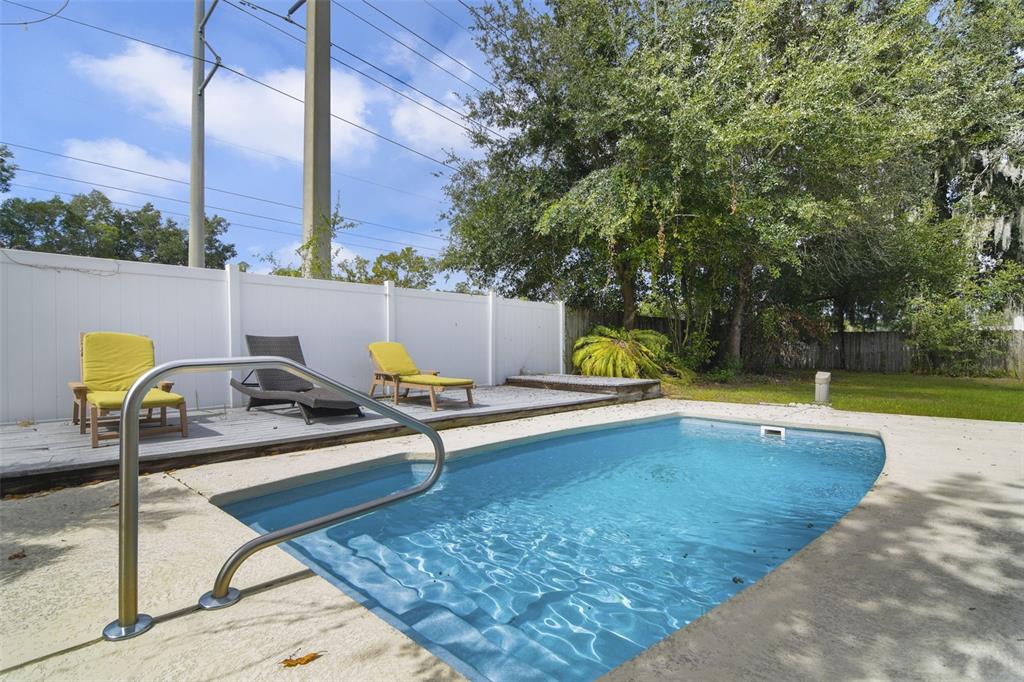 A backyard features a rectangular swimming pool, a wooden deck with lounge chairs, and fencing — 1410 SE 44TH AVENUE, OCALA, FL